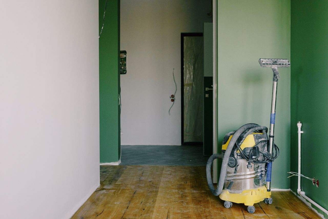 services-03 Industrial vacuum cleaner placed on dirty parquet in room with green walls and doorway in spacious apartment during repair works